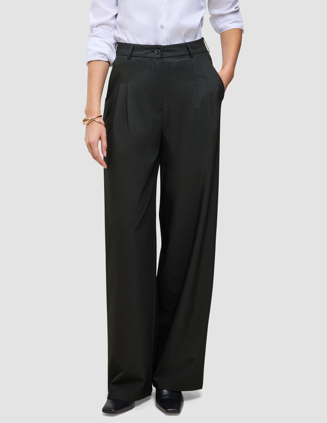 En person som har på seg svarte Avira Pants Wide for damer og en hvit skjorte med knapper.